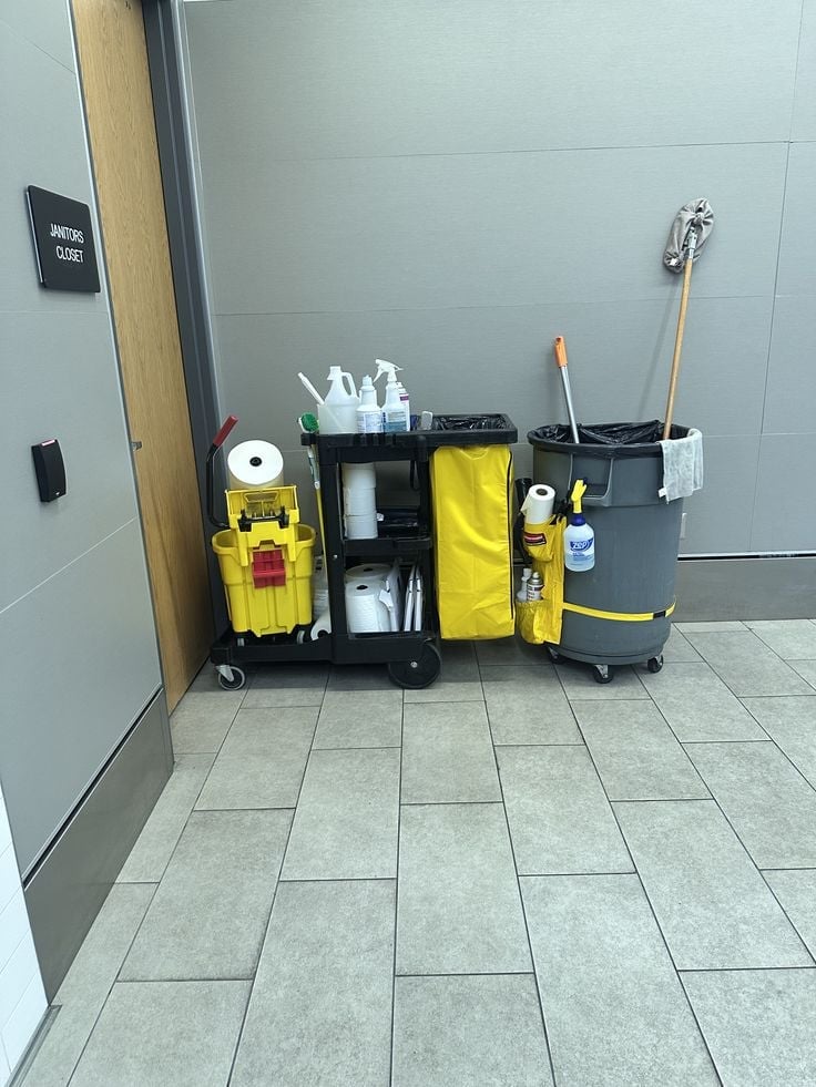 Janitorial cleaning cart staged outside a Janitors Closet at a commercial property — mop, broom, spray bottles and supplies organized on a clean tile floor